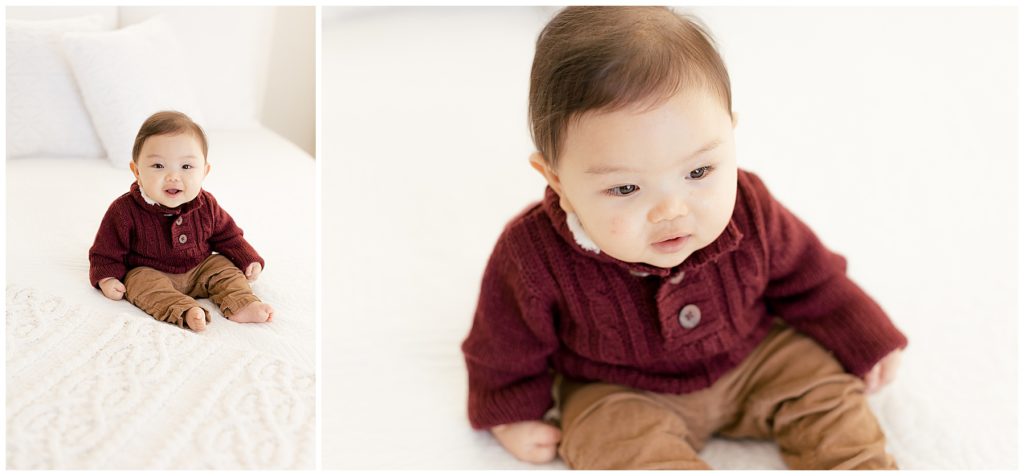 baby in burgundy sweater and brown cords on white bed