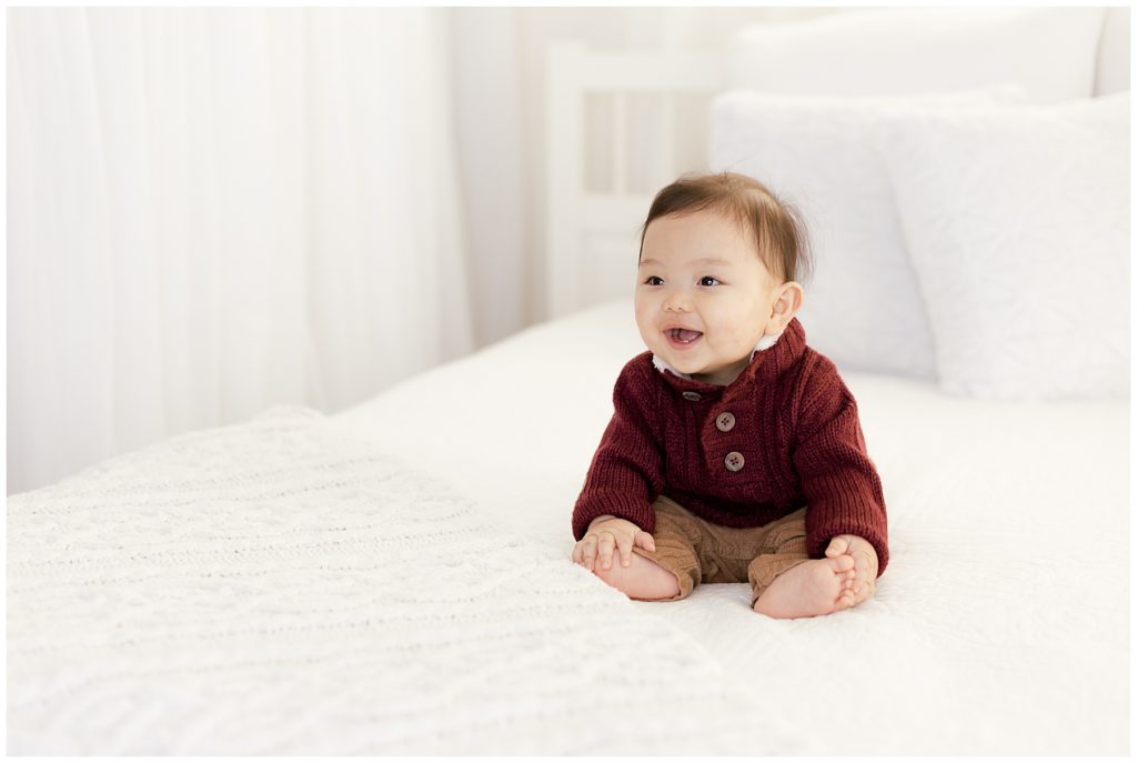 baby laughs at dad while sitting on white bed