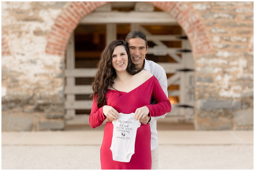smiling pregnant couple holds Covid onesie
