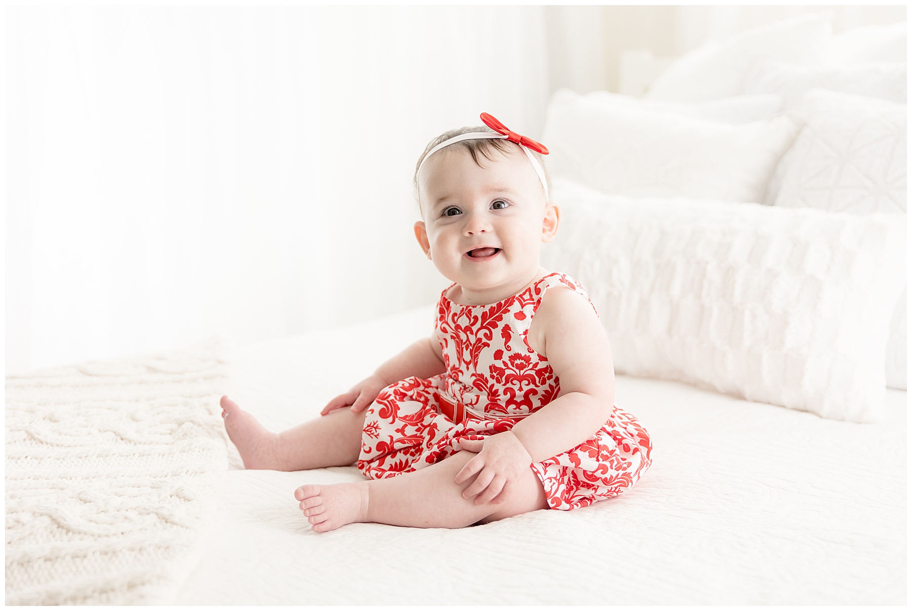 baby in red sits on white bed, watching baby grow