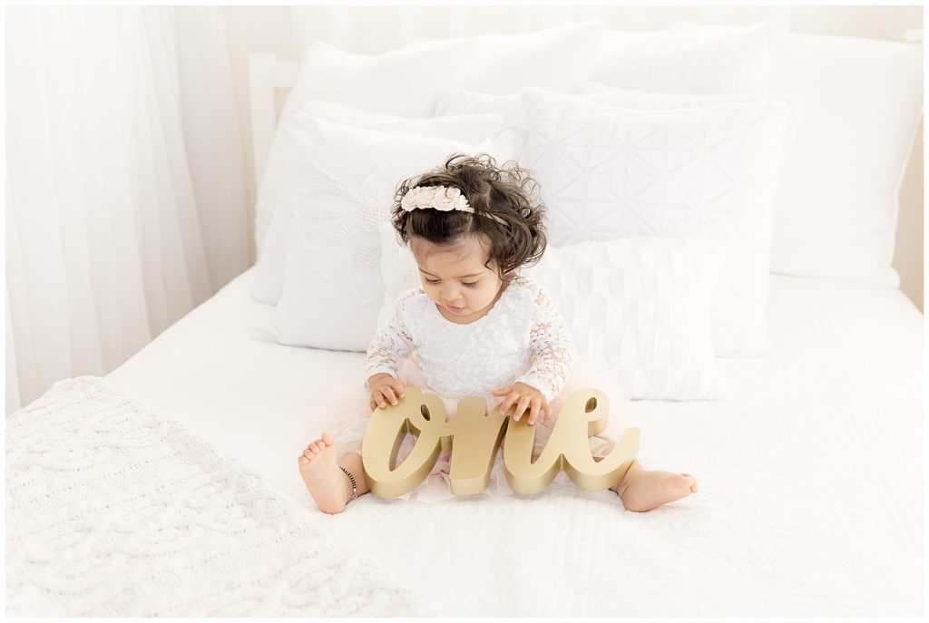 baby on white bed stares at one letters