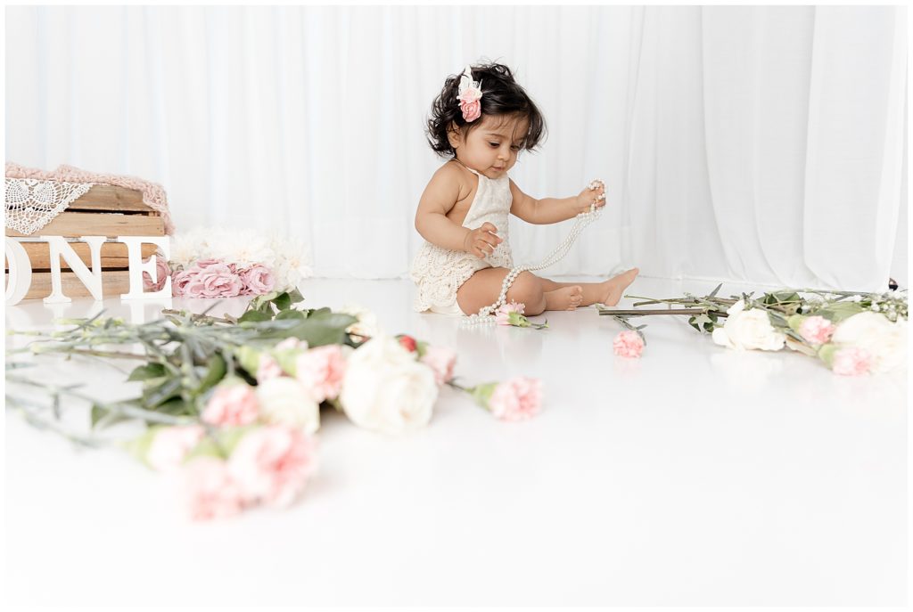 baby sits amidst flowers and pearls