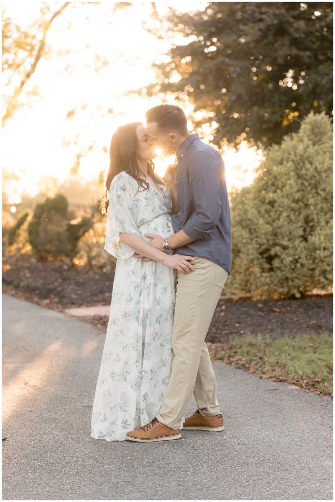 pregnant couple kisses with sunflare