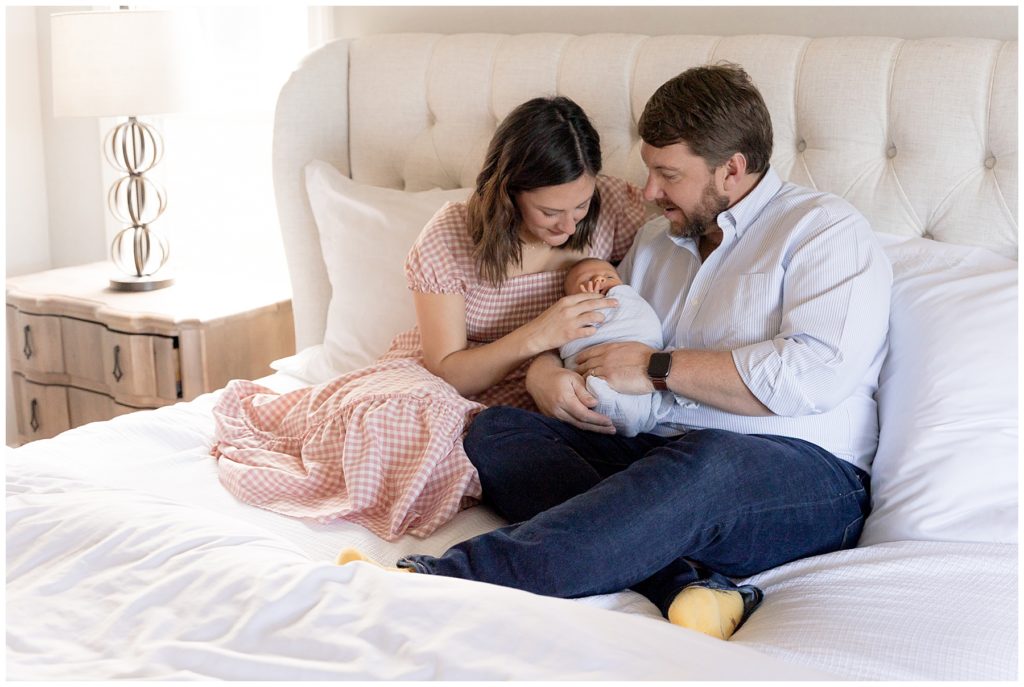 husband and wife sit on master bed with newborn son