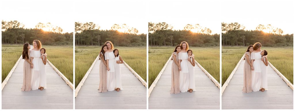mom stands on boardwalk with daughters at sunset