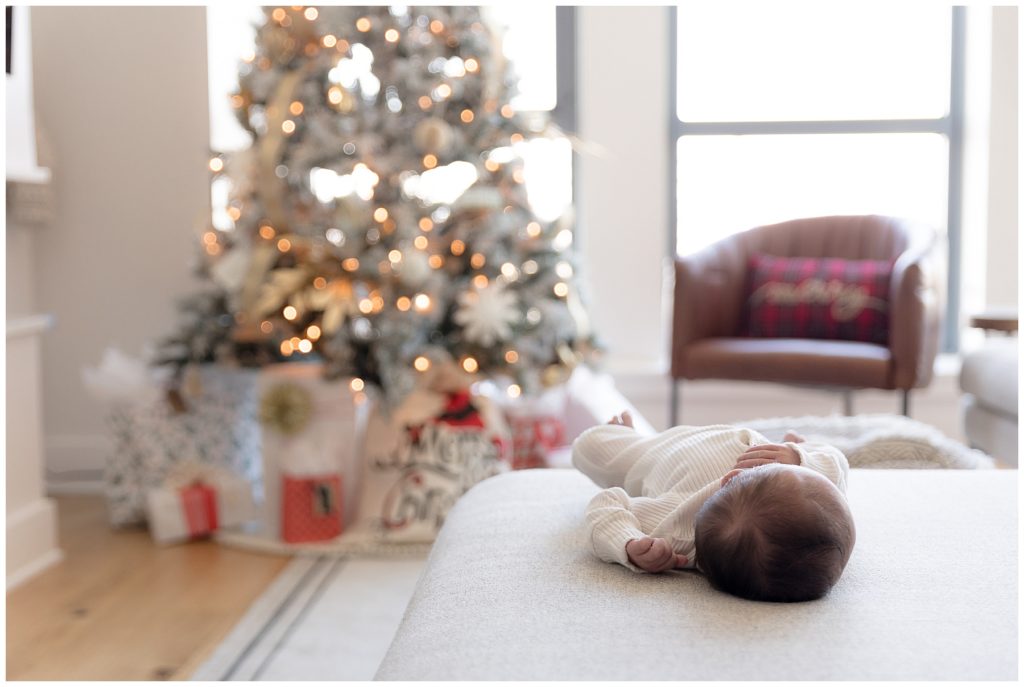 newborn lays on ottoman by Christmas tree