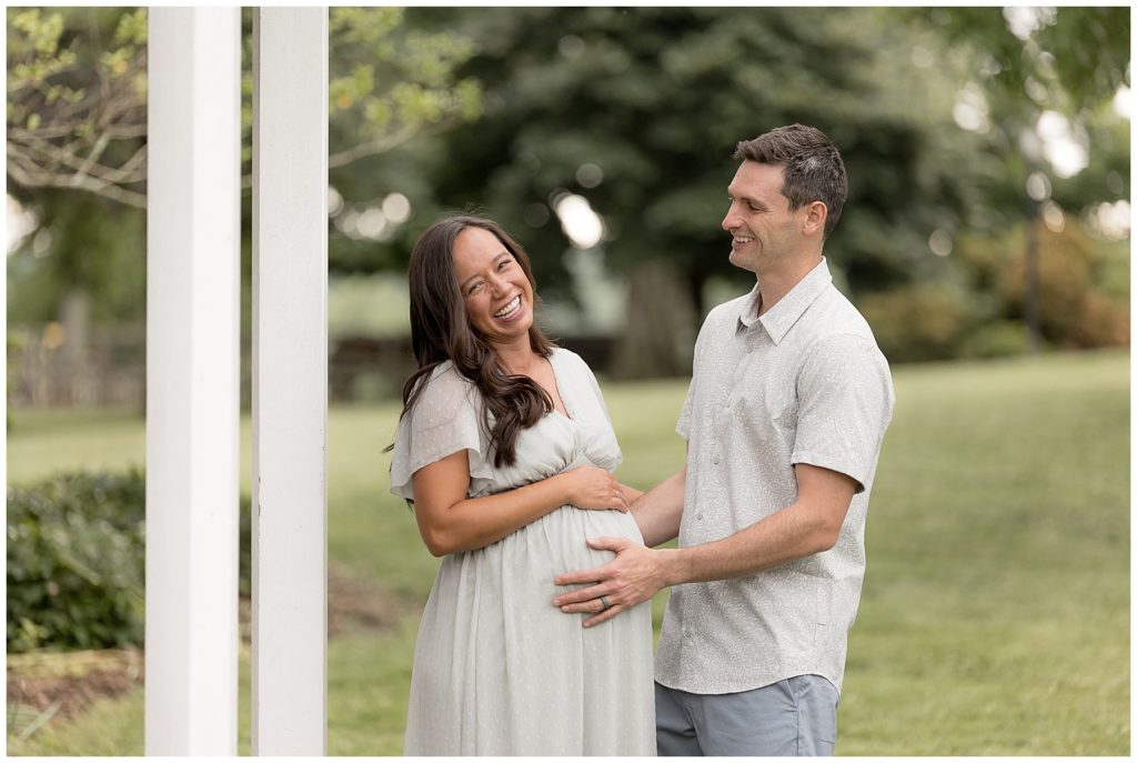 wife laughs while husband gazes at her with his hand on her pregnant belly
