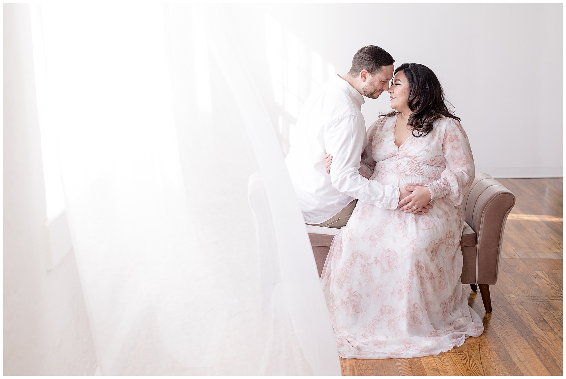breeze blows sheer curtains over posed pregnant couple