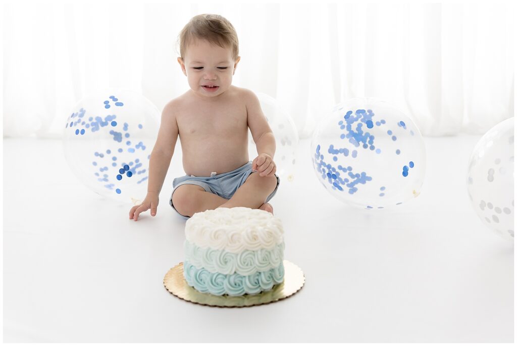 Baby makes a dismayed face as he looks at his birthday smash cake.