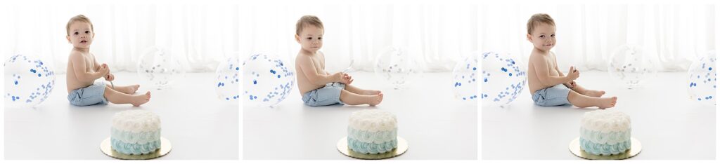 Boy in blue shorts hold a fork as he gazes at his untouched birthday smash cake and shoots an impish grin at the camera.