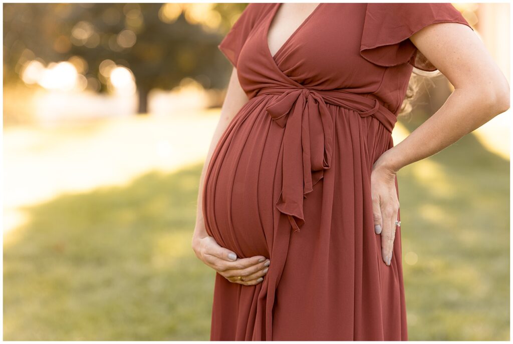 Zoomed in shot of a pregnant belly, beautifully draped by a rust-colored maternity dress