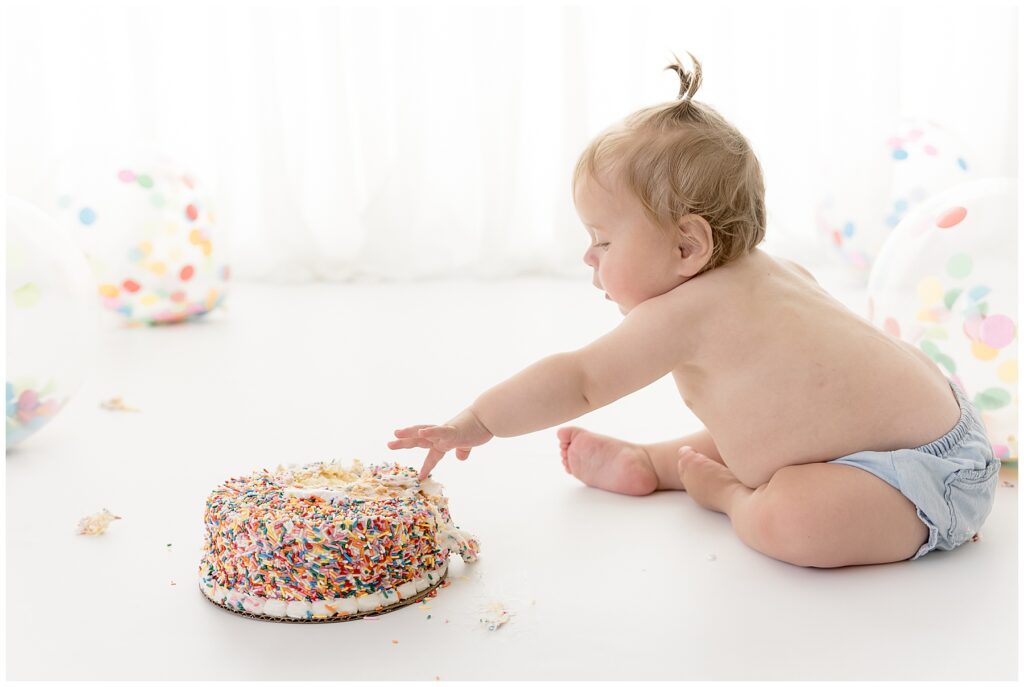 messy baby reaches for her sprinkle-covered birthday cake