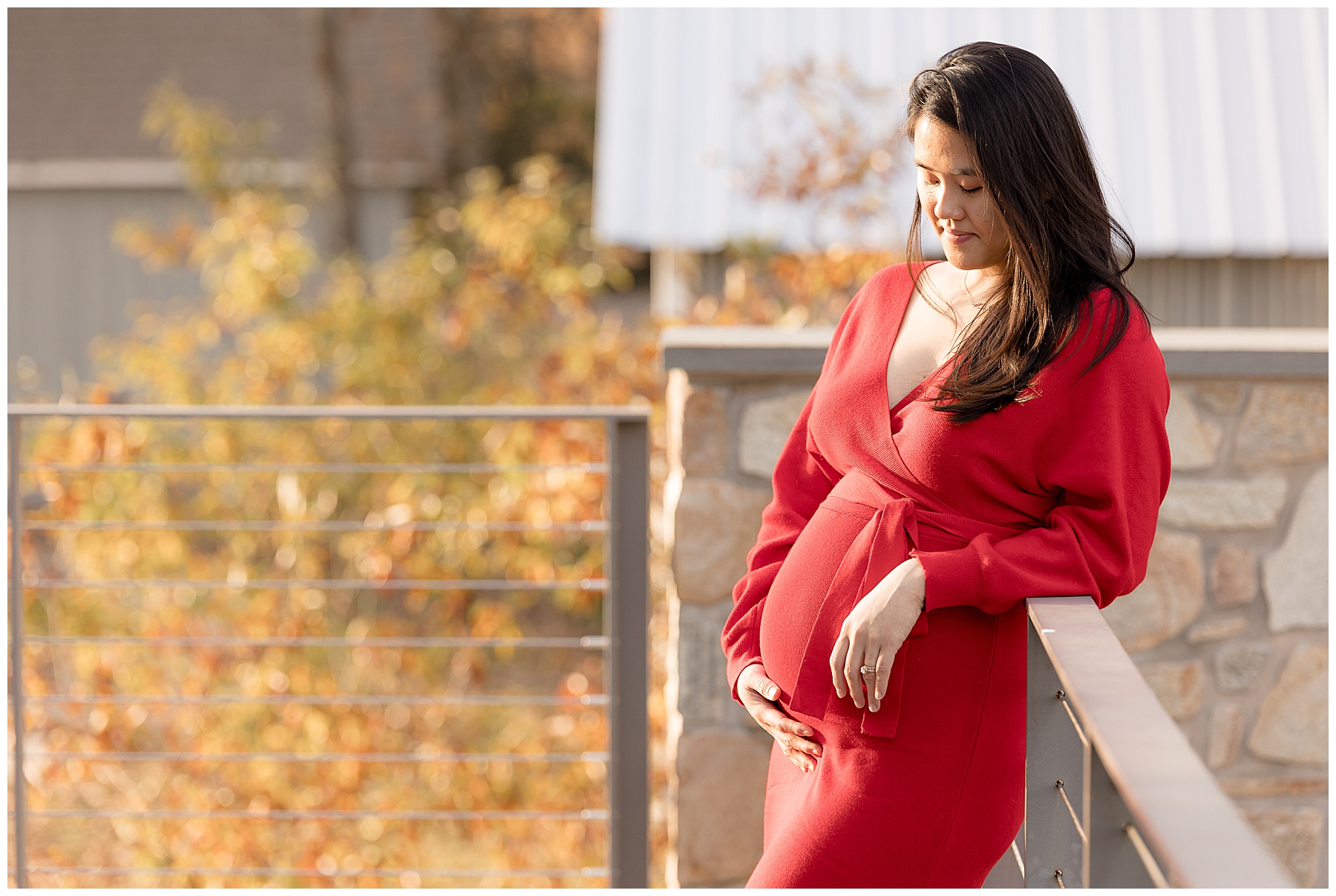 gorgeous pregnant woman in red dress stands on a rooftop deck in a beam of sunshine