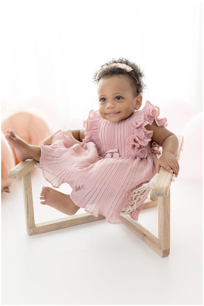 baby girl props her feet up on her chair and smiles during her birthday photo session