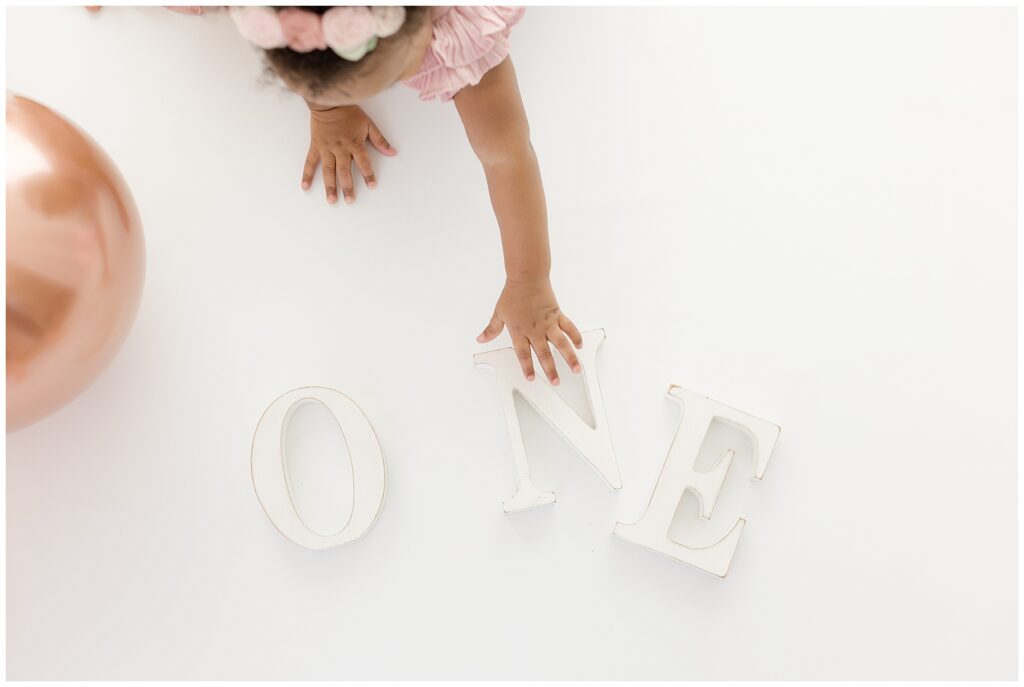 a little girl's hand reaches for wooden letters that spell out ONE during her birthday photo session