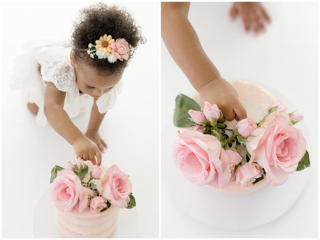 baby girl reaches for her birthday cake which is covered in pink roses