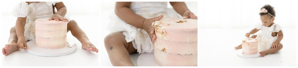baby girl sits on white flooring and plays with her pink birthday cake