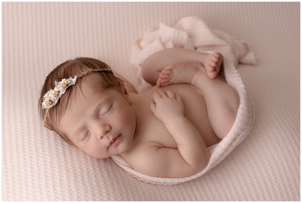 Tiny newborn baby girl snuggled in the egg wrap pose with her legs curled up and her hand resting on her chest.