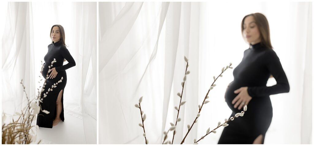Pregnant woman in fitted black dress against white curtained backdrop with foliage.